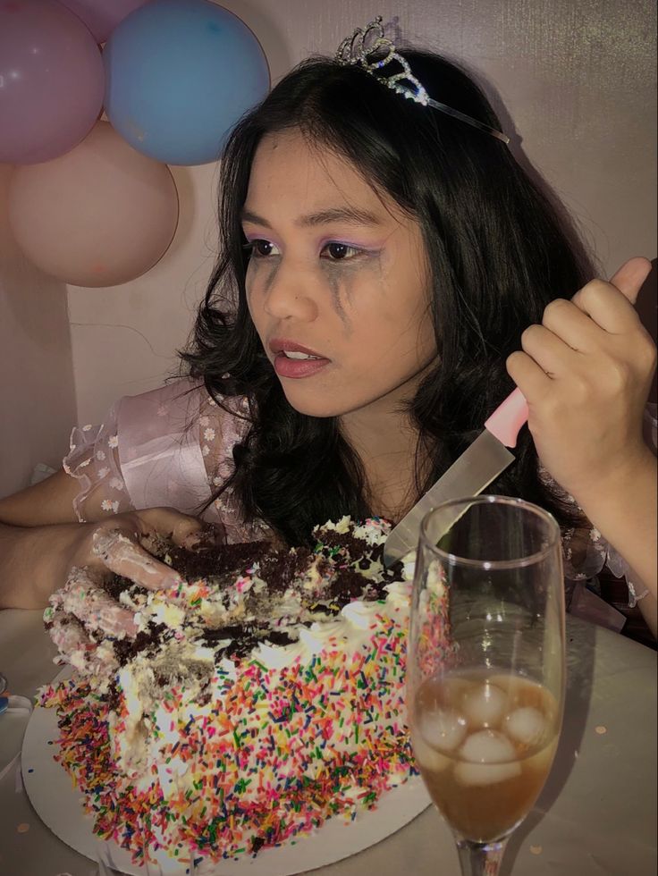 a woman is cutting into a birthday cake with a knife and fork, surrounded by balloons and confetti