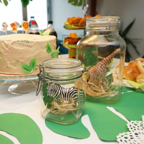 there is a cake in the glass jar on the table with zebras and giraffe figurines