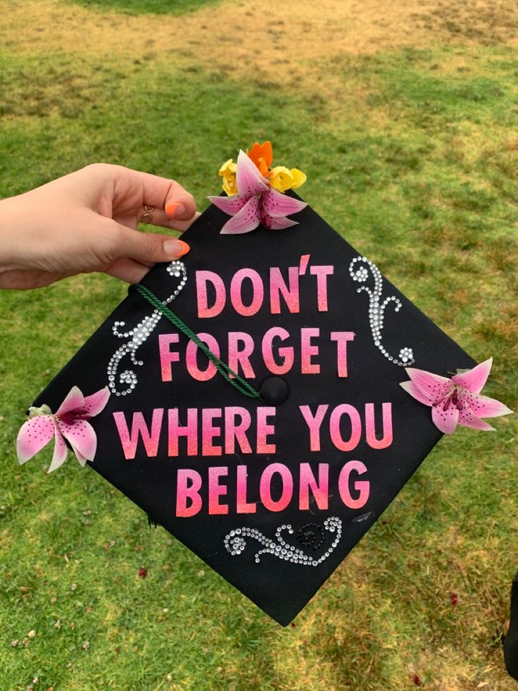 a person holding a black graduation cap with pink flowers on it that says, don't forget where you belong