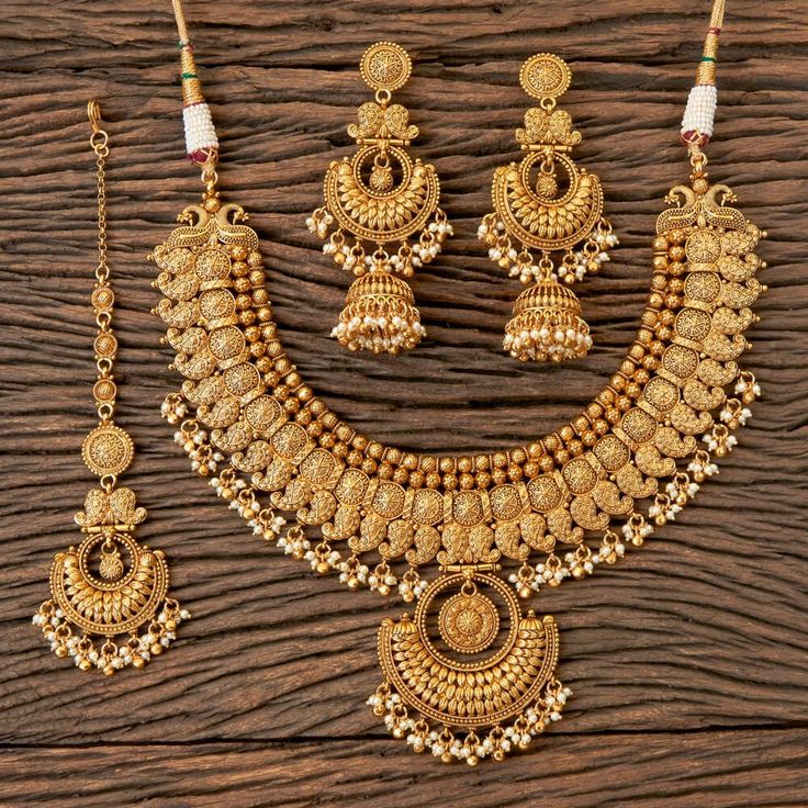 a gold necklace and earring set on a wooden surface, with beads hanging from it