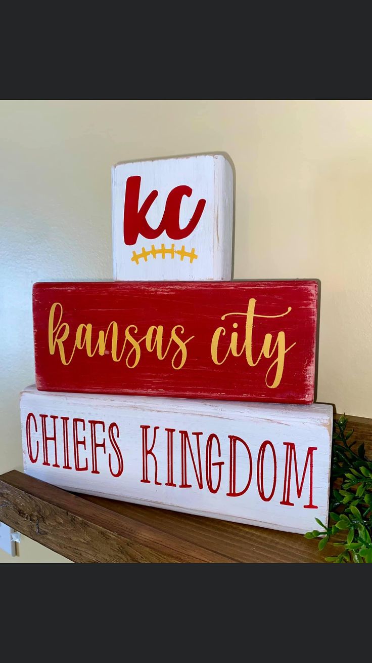 three wooden signs are stacked on top of each other, one has kansas city and the other says chiefs kingdom