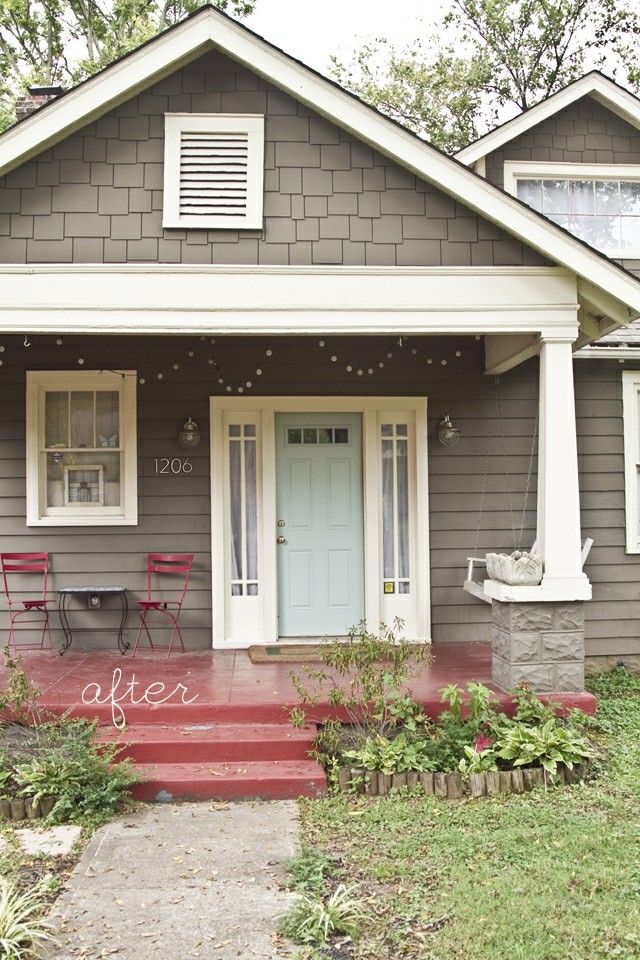 a gray house with red steps leading up to the front door and two chairs on the porch