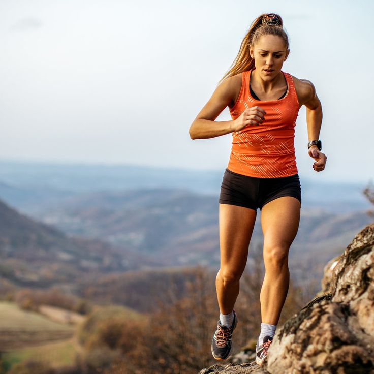 a woman running on top of a rocky hill in an orange shirt and black shorts