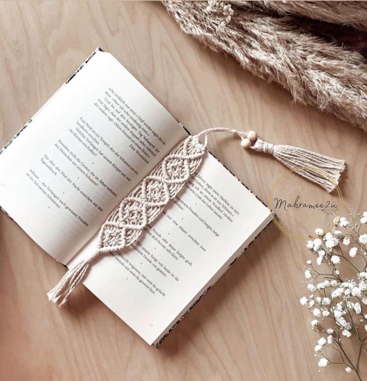 an open book sitting on top of a wooden table next to a vase with flowers