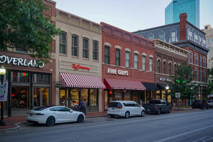 several cars are parked on the street in front of some shops and stores at dusk