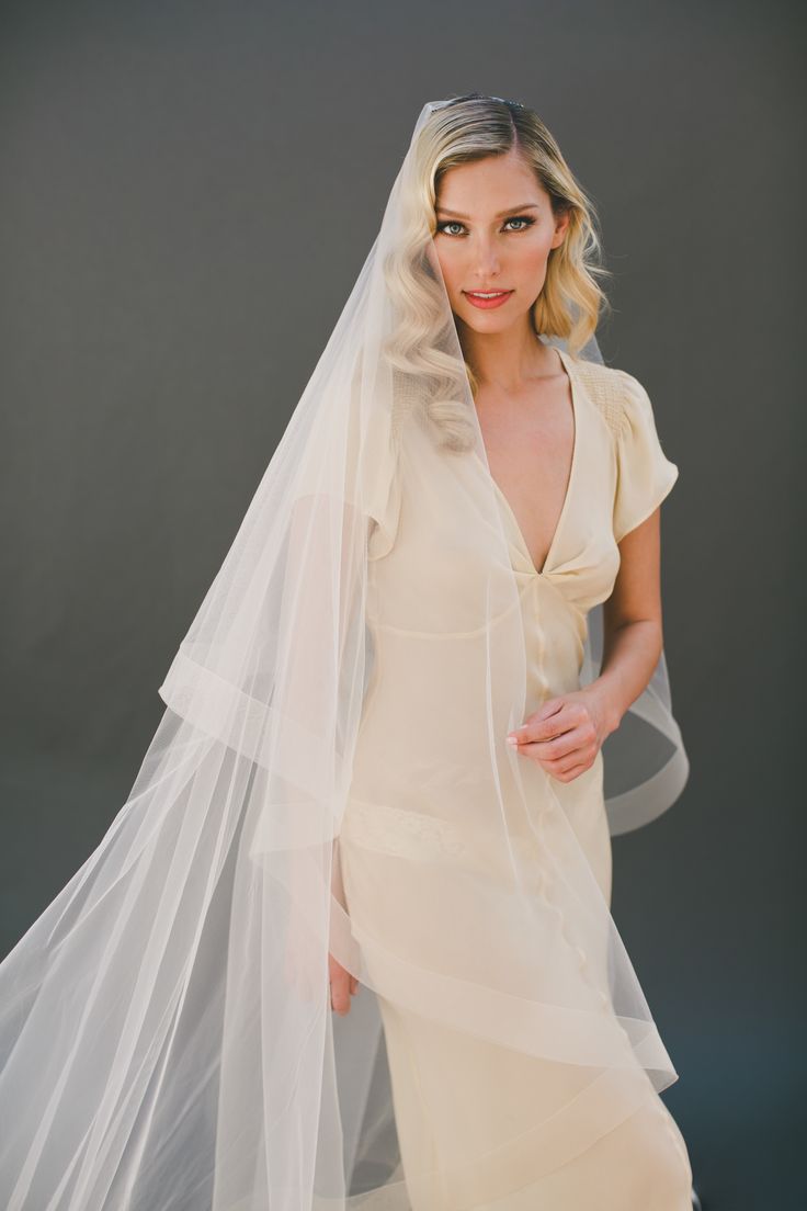 a woman in a wedding dress and veil posing for the camera with her hands on her hips