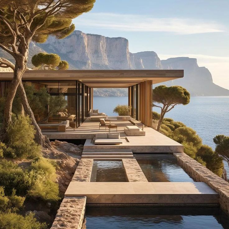 an outdoor swimming pool next to the ocean with trees and mountains in the background at sunset