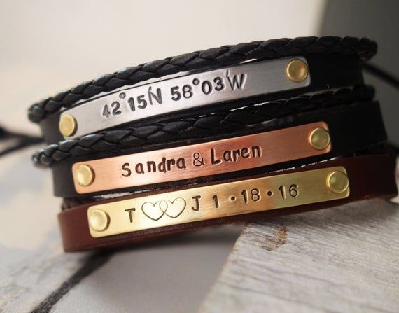 three personalized leather bracelets with gold and silver engraving on black cord, one for the couple's names