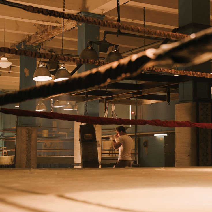 a man standing in a boxing ring talking on his cell phone with ropes hanging from the ceiling