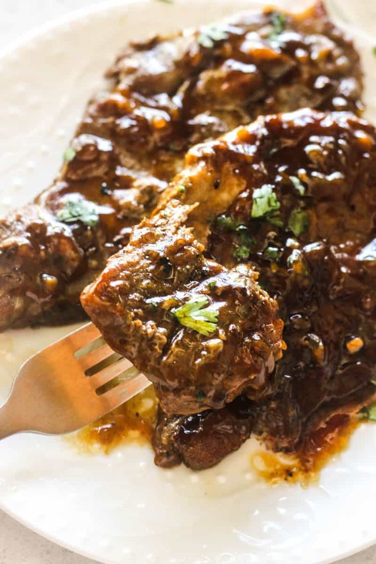 a white plate topped with meat covered in sauce and garnished with parsley