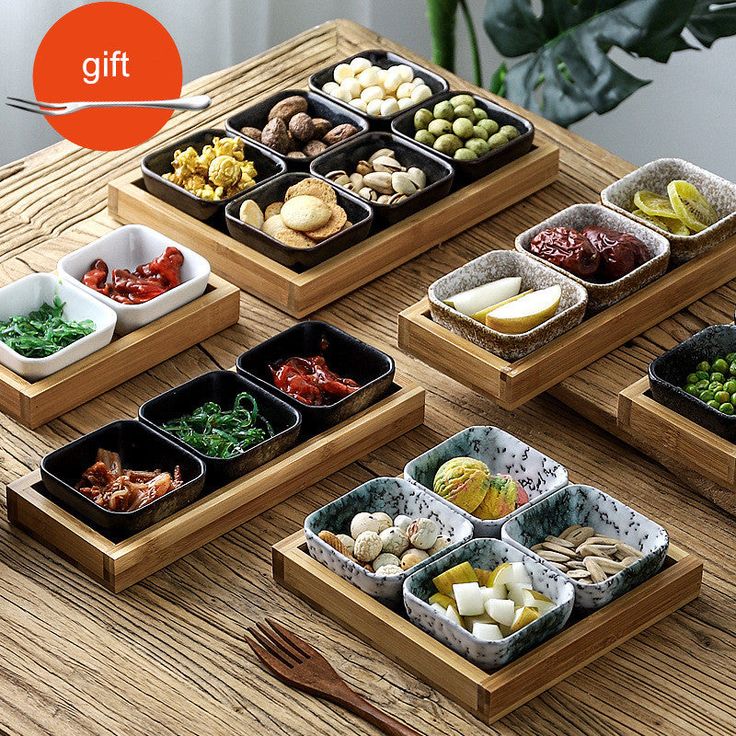 four trays filled with different types of food on top of a wooden table next to utensils