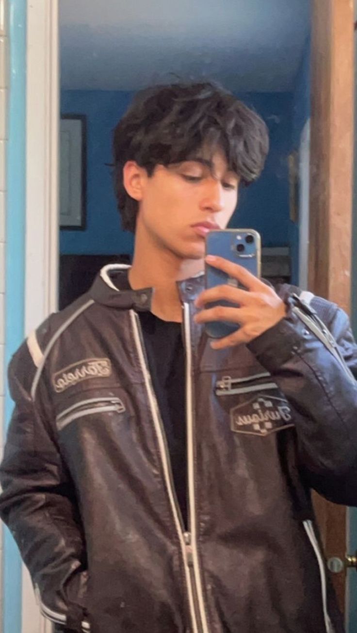 a young man in a leather jacket looking at his cell phone and taking a selfie