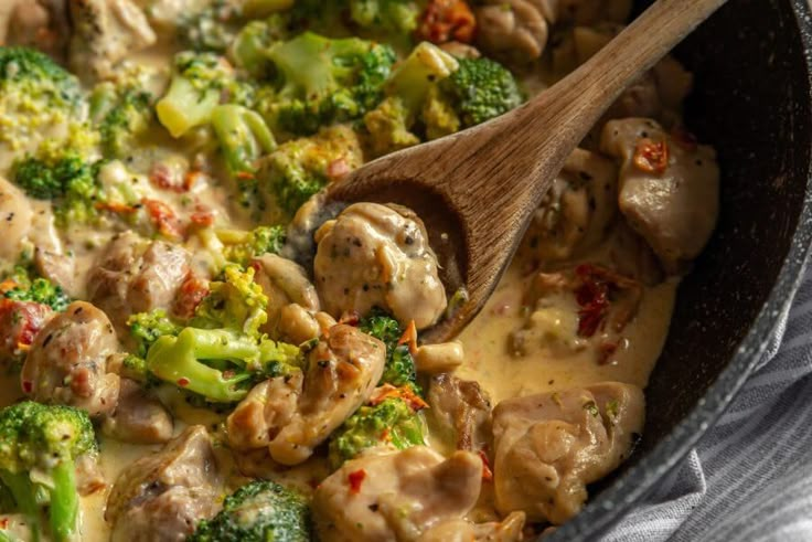 a skillet filled with broccoli and meat covered in gravy next to a wooden spoon