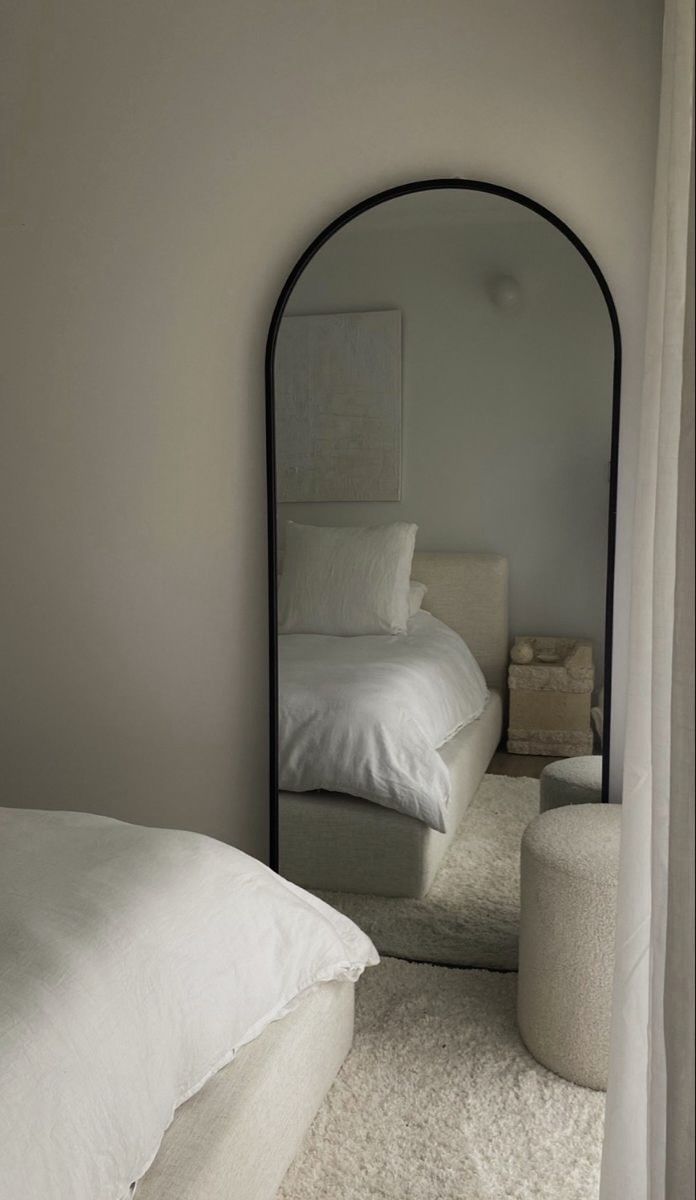 a white bed sitting under a mirror in a bedroom