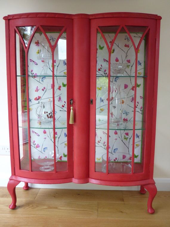 a red china cabinet with glass doors and flowers on it