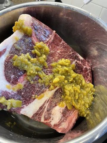 a piece of meat in a pot with some green stuff on the top and yellow mustard on the bottom