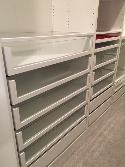 there are many drawers in the closet with white shelves on each side and red bins at the bottom