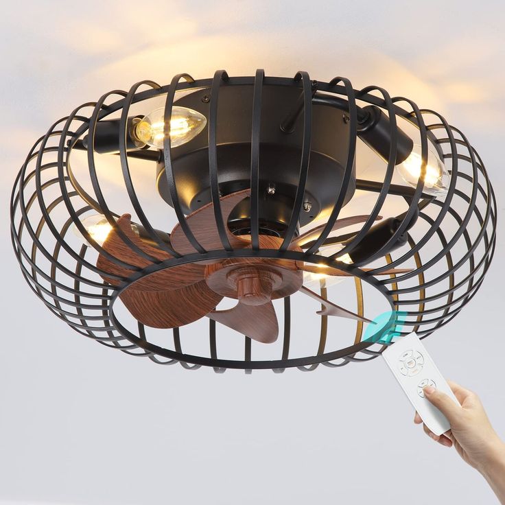 a person holding a remote control in front of a ceiling fan with caged design