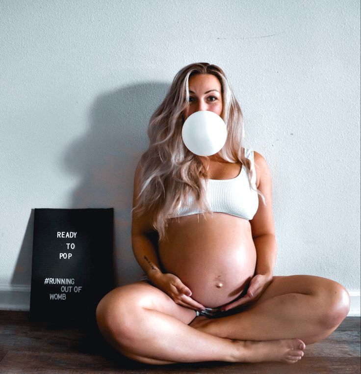 a pregnant woman is sitting on the floor with a pacifier in her mouth while she holds out her belly