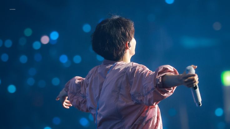 a man holding a microphone in his right hand and wearing a pink shirt on stage