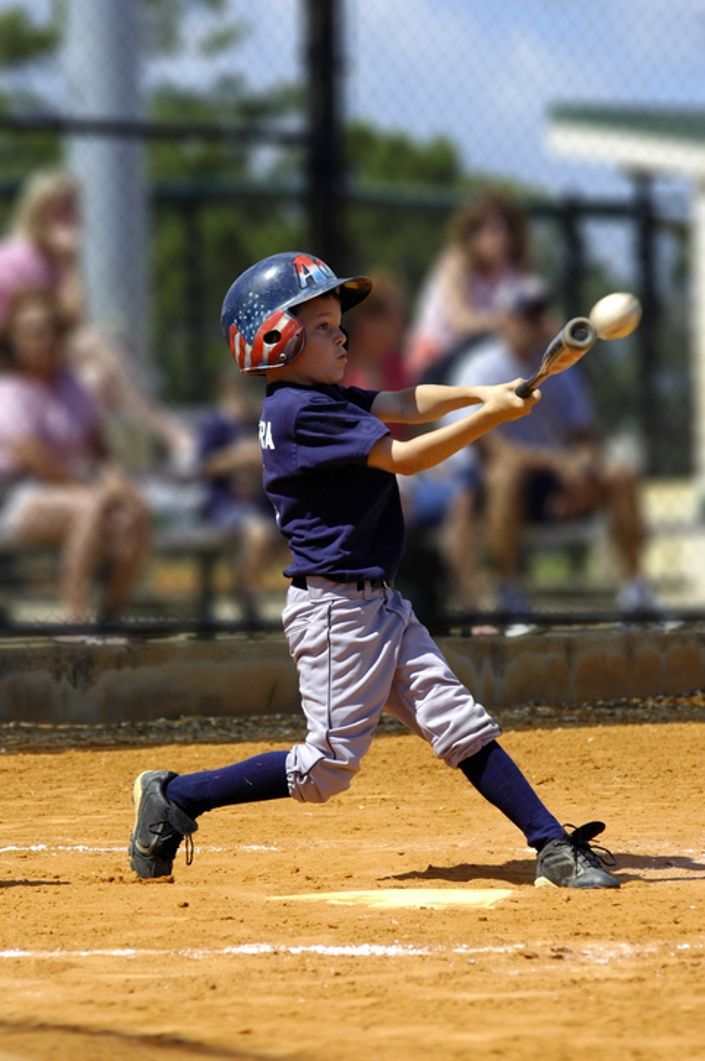 a young boy swinging a baseball bat at a ball on a field with spectators in the background