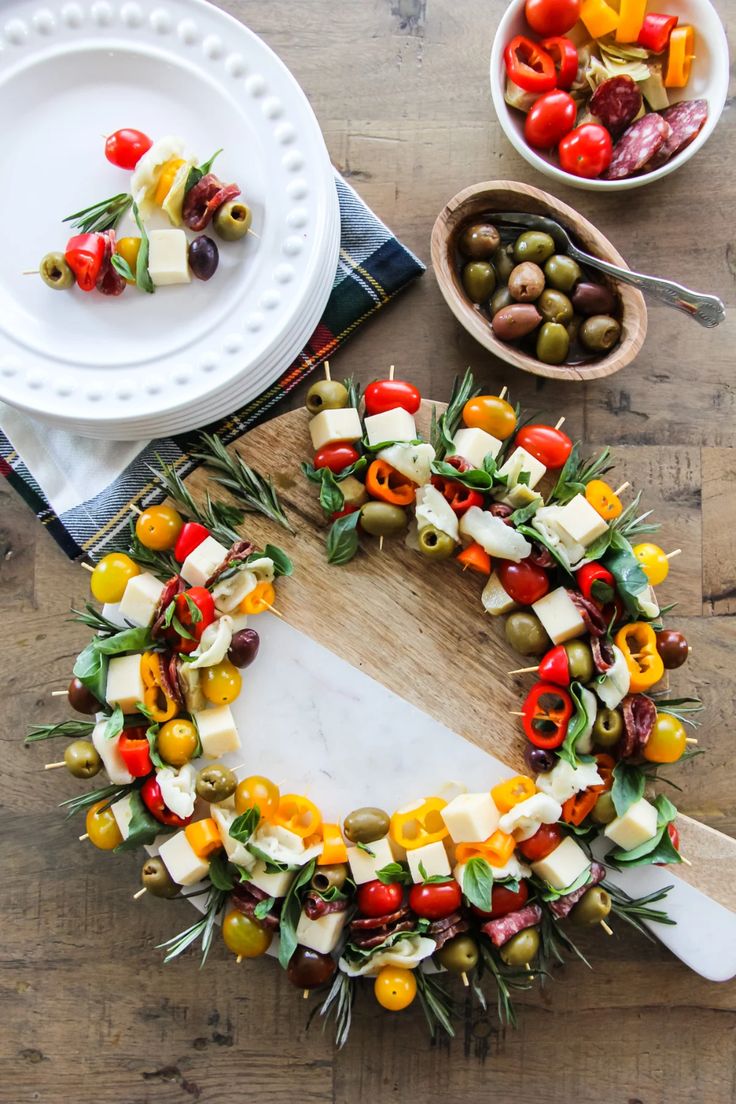 a wreath made out of olives, peppers and cheese on a cutting board next to other foods