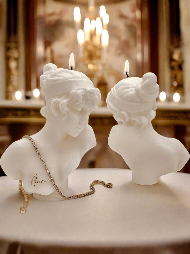 two white busturines sitting on top of a table with candles in the background