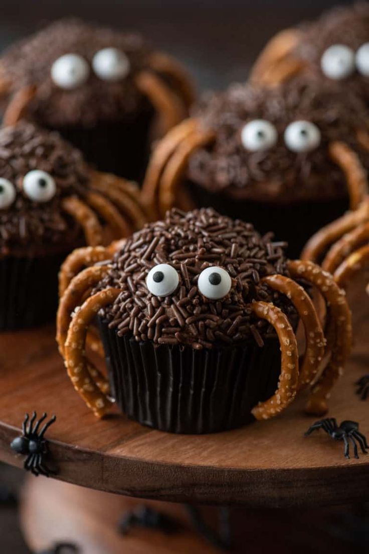 chocolate cupcakes decorated with googly eyes and spider legs on a wooden platter