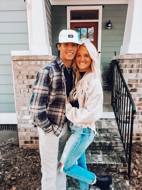 a man and woman standing in front of a house with their arms around each other