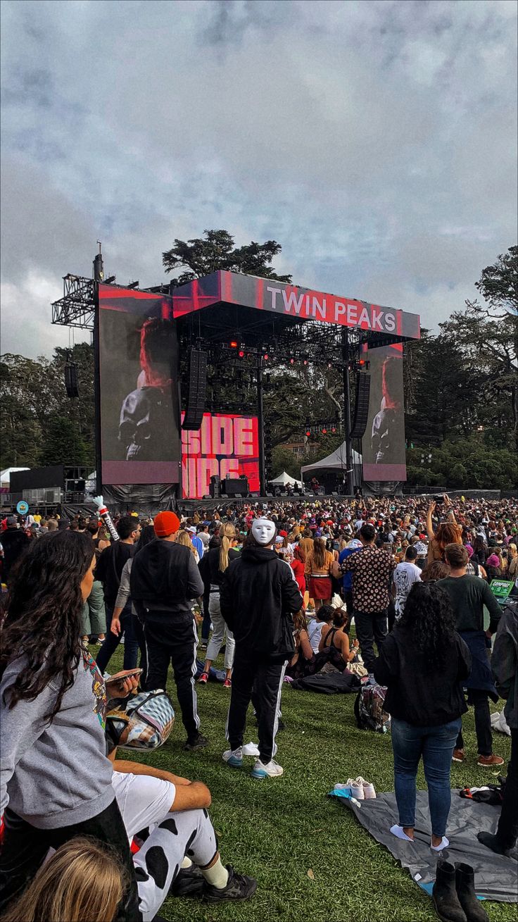 a large group of people standing on top of a lush green field next to a giant screen