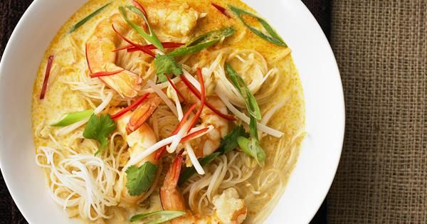 a white bowl filled with noodles and shrimp on top of a black place mat next to a cup of coffee