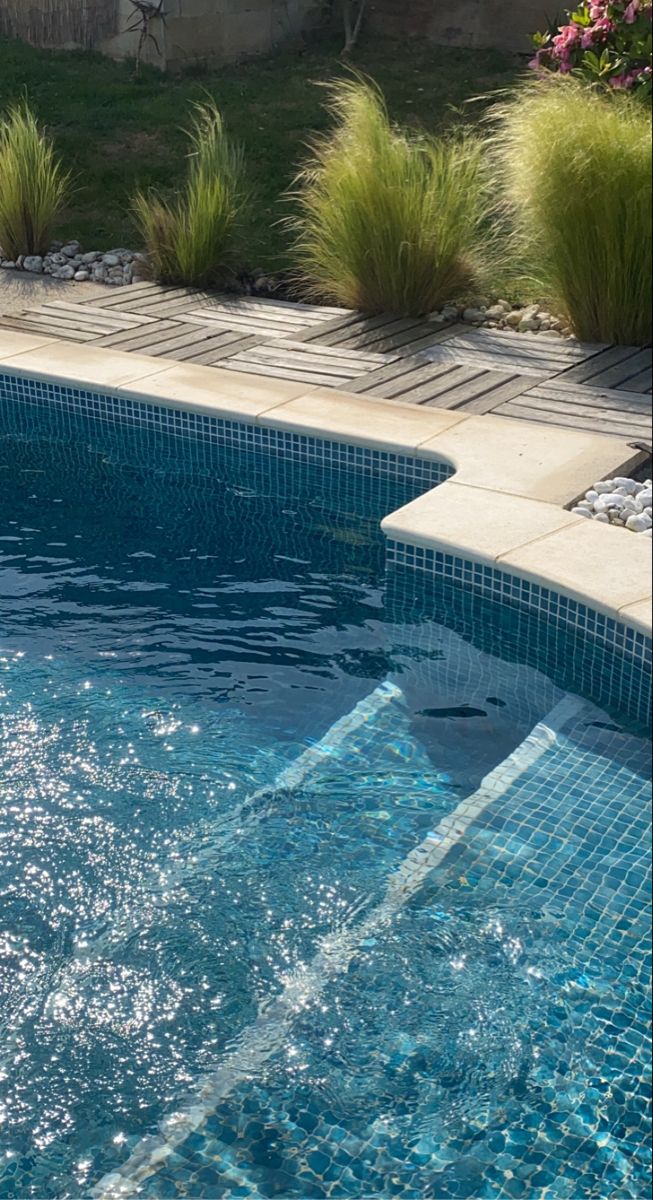 an empty swimming pool surrounded by grass and flowers