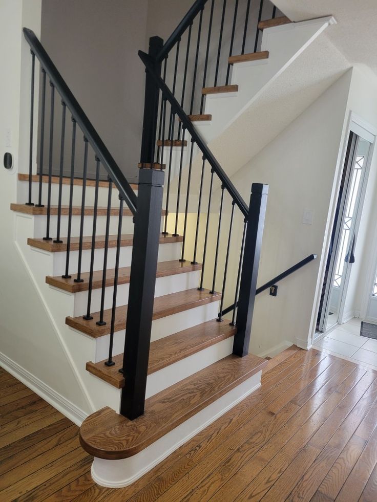 a staircase with black railing and wooden handrails in a white house, showing the wood flooring