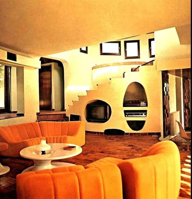 a living room with orange couches and white tables in front of a television set