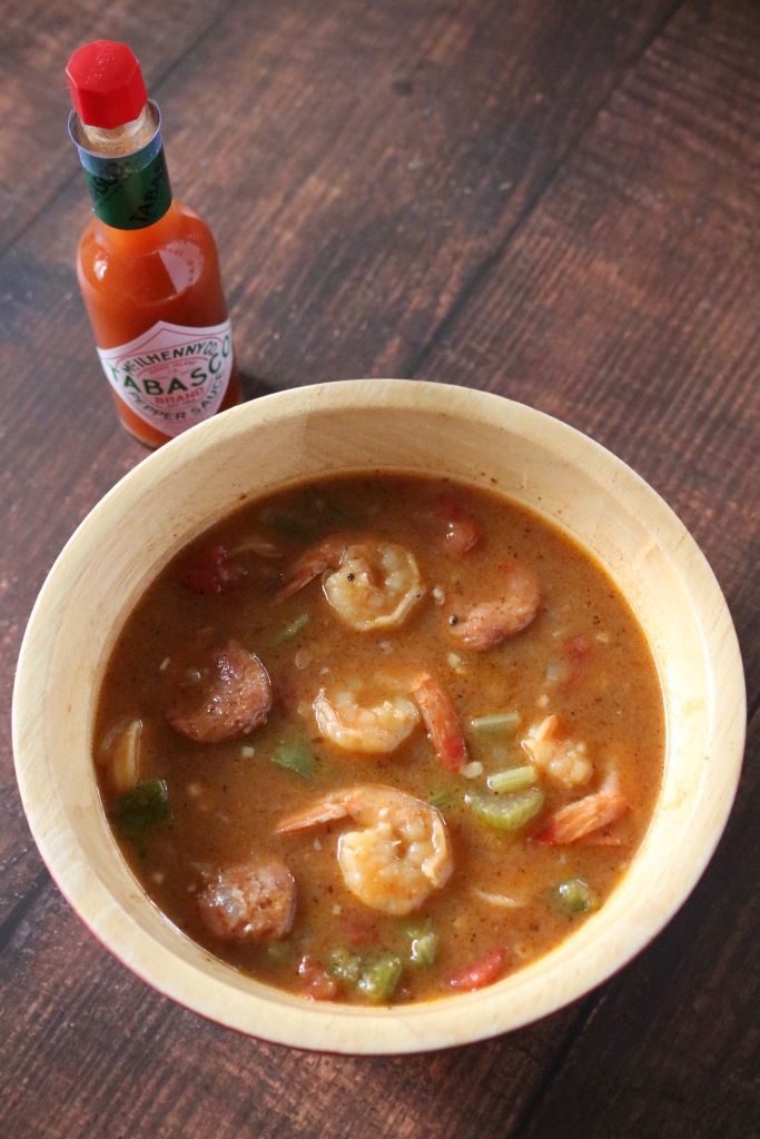 a bowl of shrimp and vegetable soup next to a bottle of hot sauce