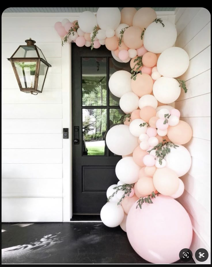 a bunch of balloons hanging from the side of a door with greenery on it