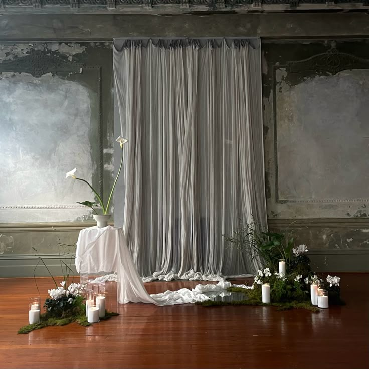 an arrangement of flowers and candles on the floor in front of a curtained window