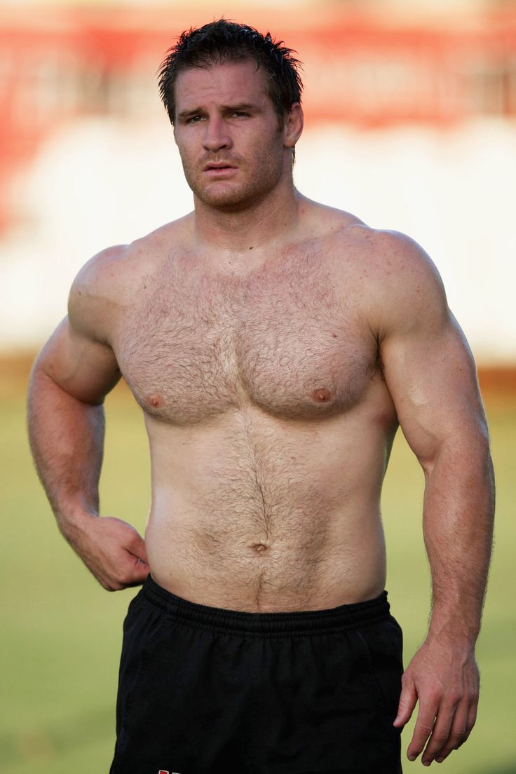 a shirtless man standing on top of a field with his hands in his pockets