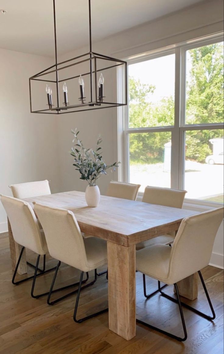 a dining room table with chairs and a vase on it in front of a large window