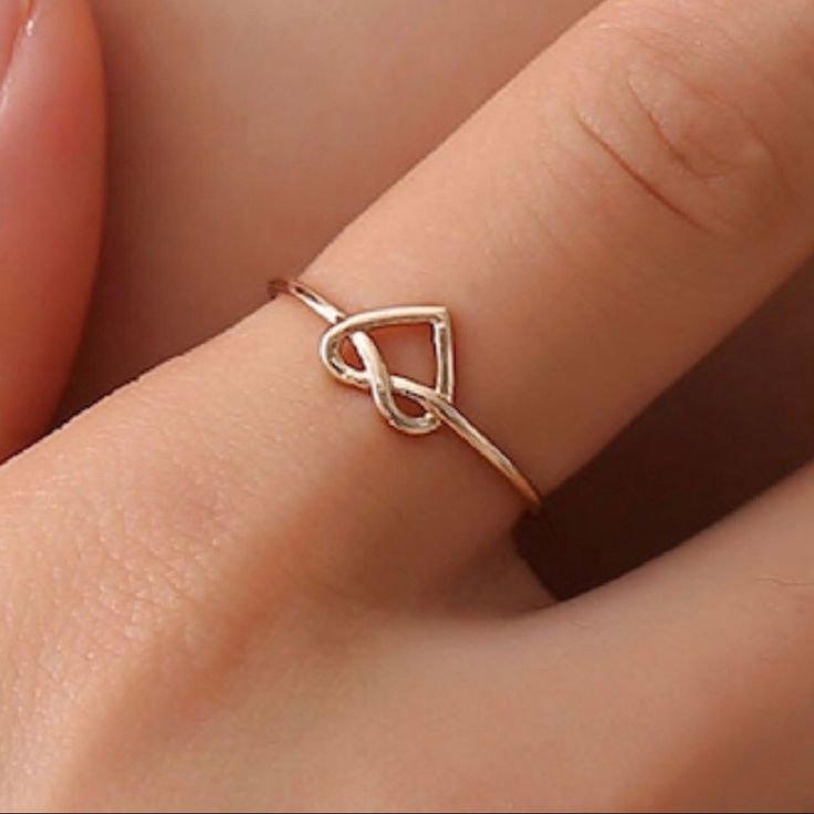 a woman's hand wearing a gold ring with a knot on the middle of it