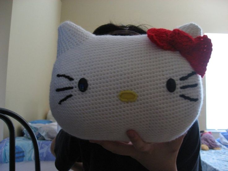 a woman holding up a crocheted hello kitty pillow in front of her face