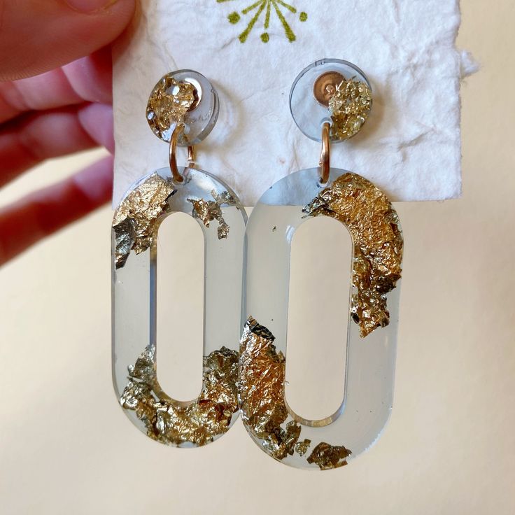 a pair of gold and white earrings on top of a piece of paper next to a napkin