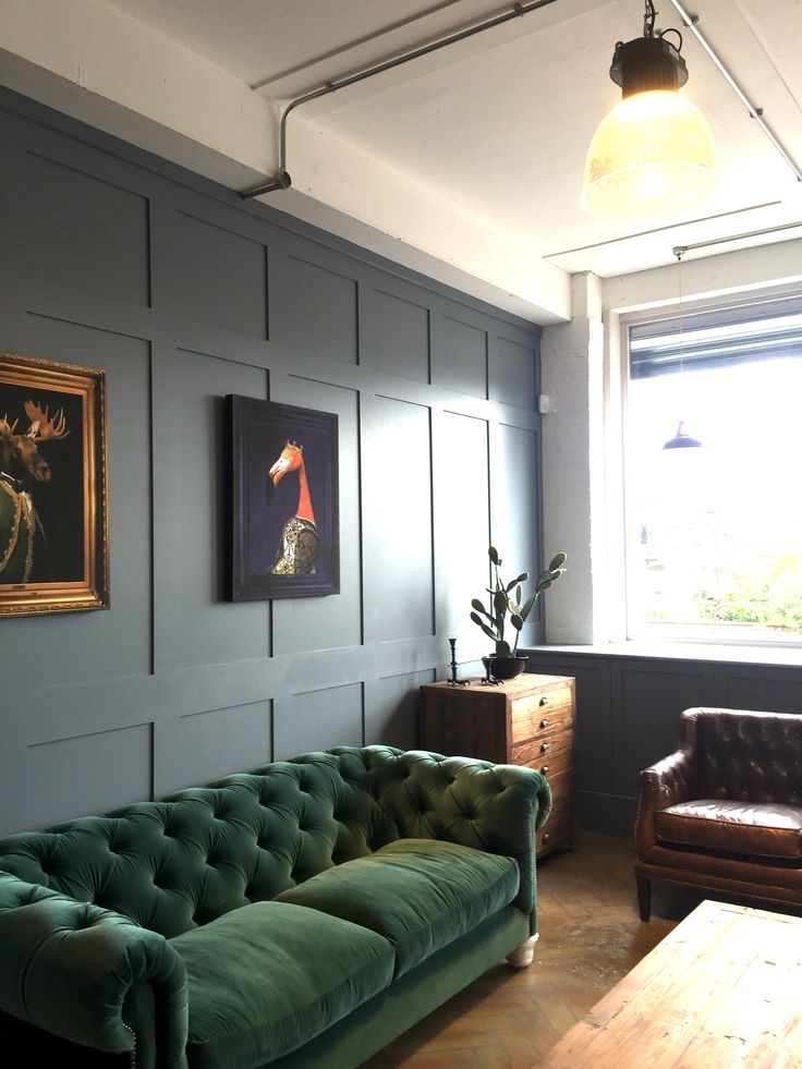 a living room with green couches and paintings on the wall above them, along with a wooden coffee table