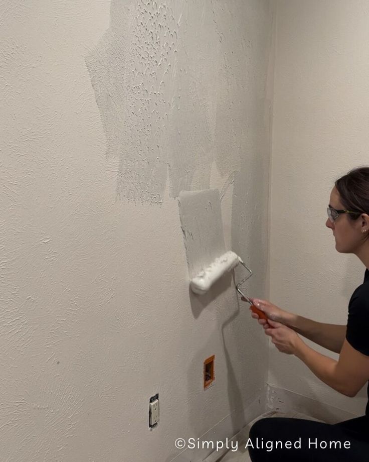 a woman is painting the wall with white paint