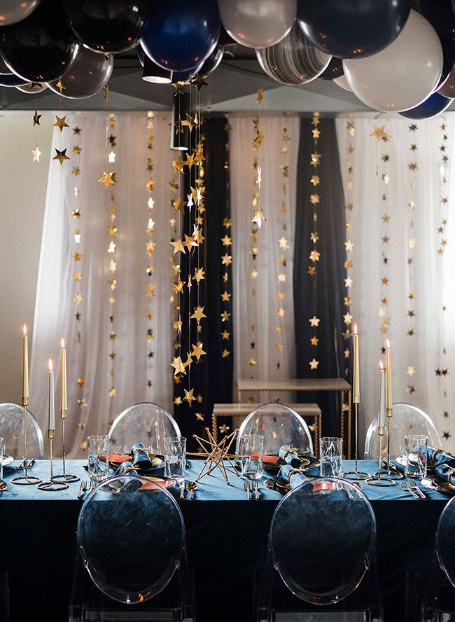 the table is set with clear chairs and black tablescloths, silver candlesticks and star - shaped balloons