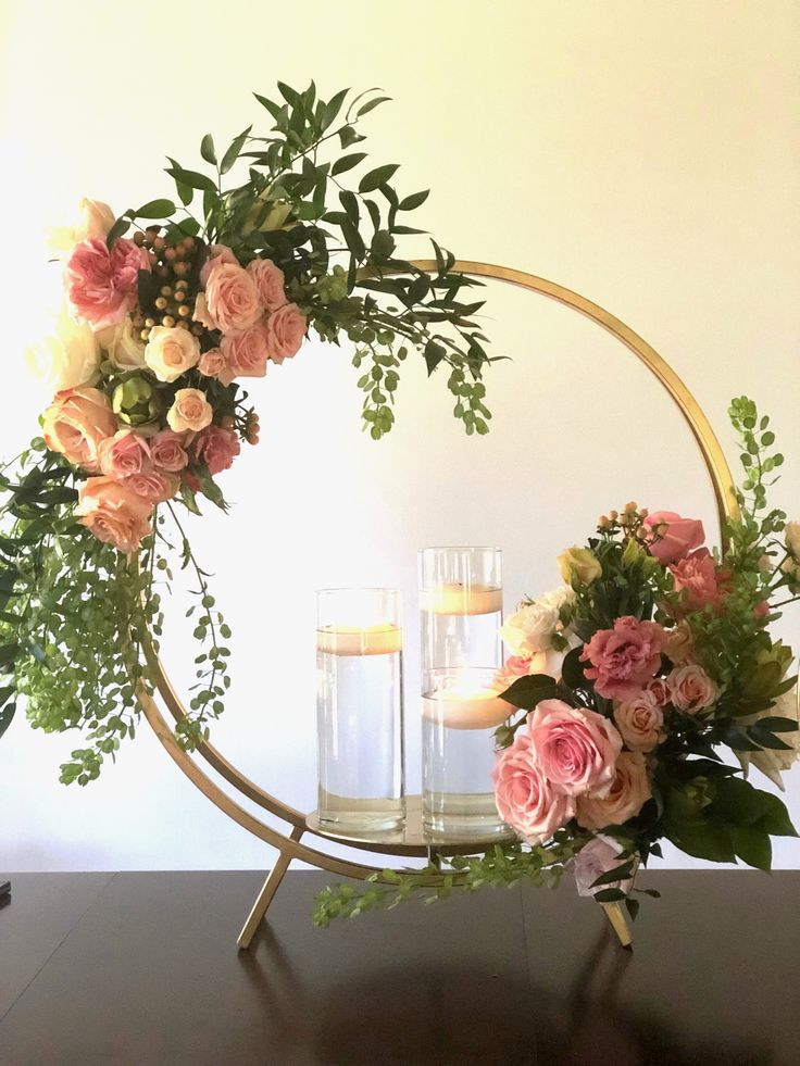 two candles are sitting in front of a floral wreath on a table with flowers and greenery