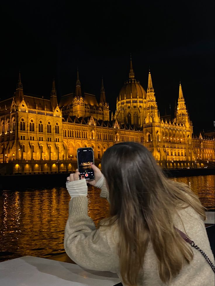 a woman taking a photo with her cell phone in front of the hungarian parliament building