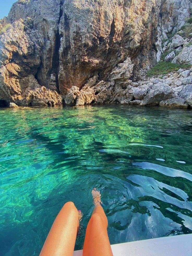 a person is sitting on a boat looking out at the water and cliffs in the background