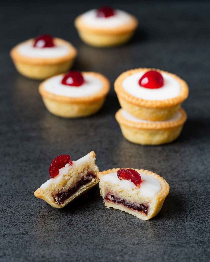 several small pastries with cherries on them sitting on a black counter top next to each other