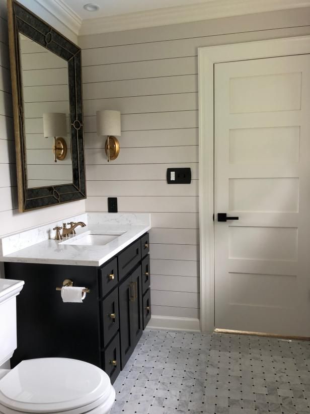 a white toilet sitting next to a black sink in a bathroom under a large mirror